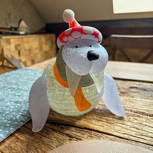 Glass figure of a walrus with a Christmas hat on a wooden table. The character named Wally wears white tusks, a scarf and radiates festive coziness.